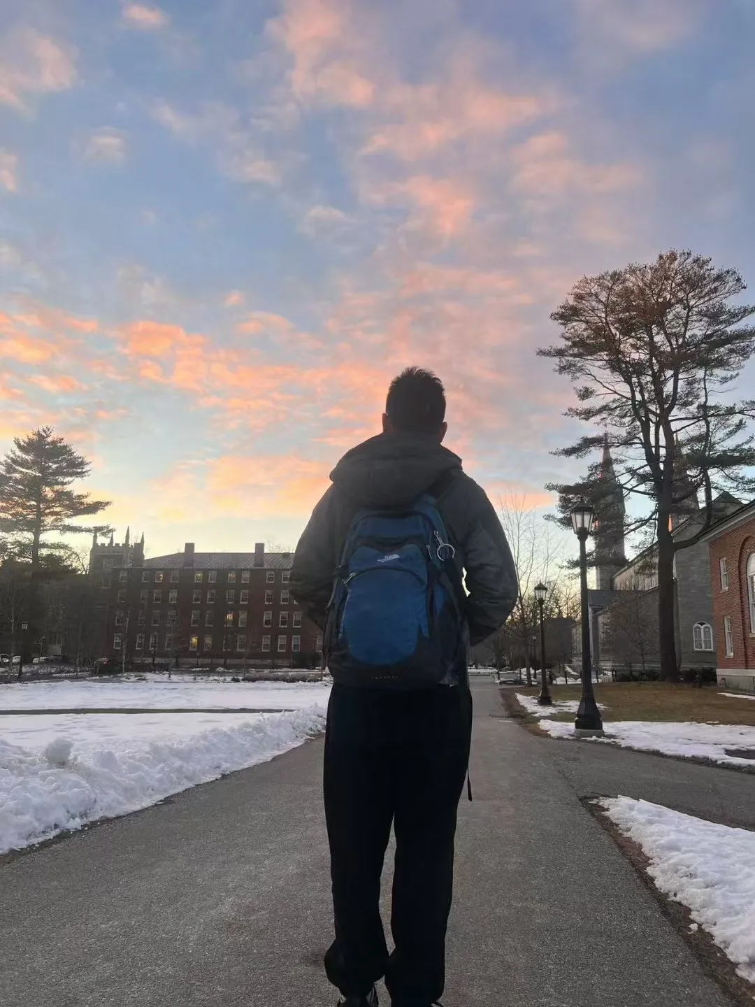Zimo walking along a snowy campus path at dusk