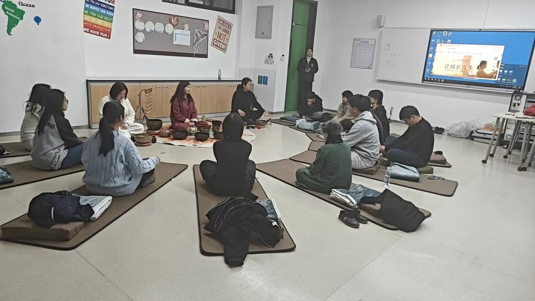 Students seated in a circle on mats around singing bowls